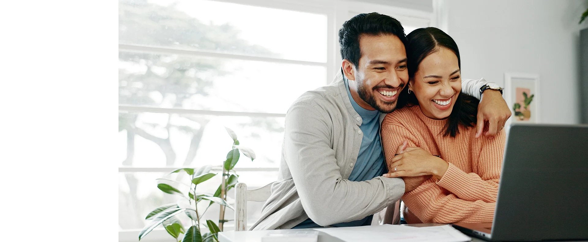 A smiling couple looks at a laptop screen together at home.